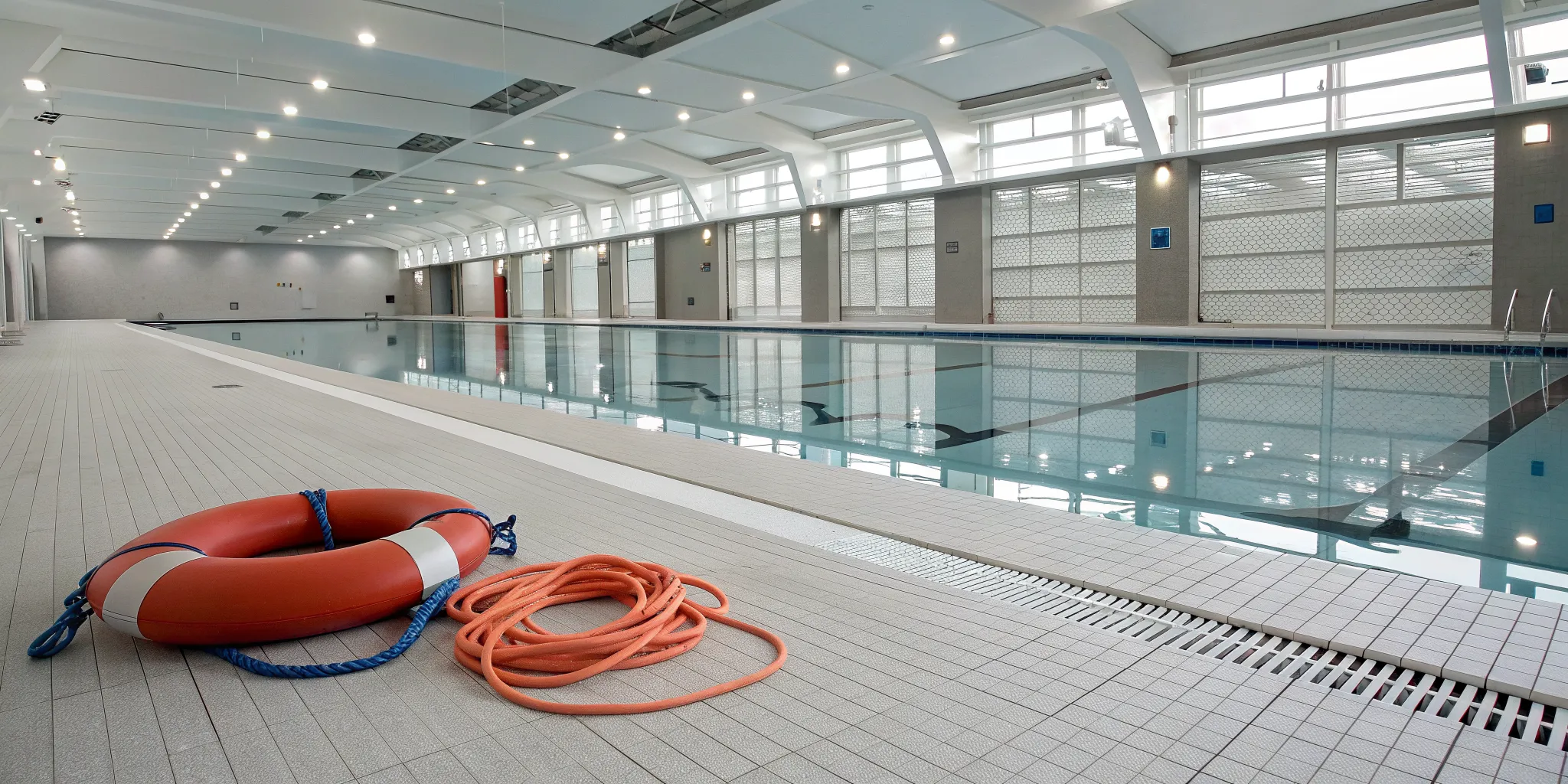 Commercial pool safety equipment, including a life ring and rescue rope, on a pool deck.