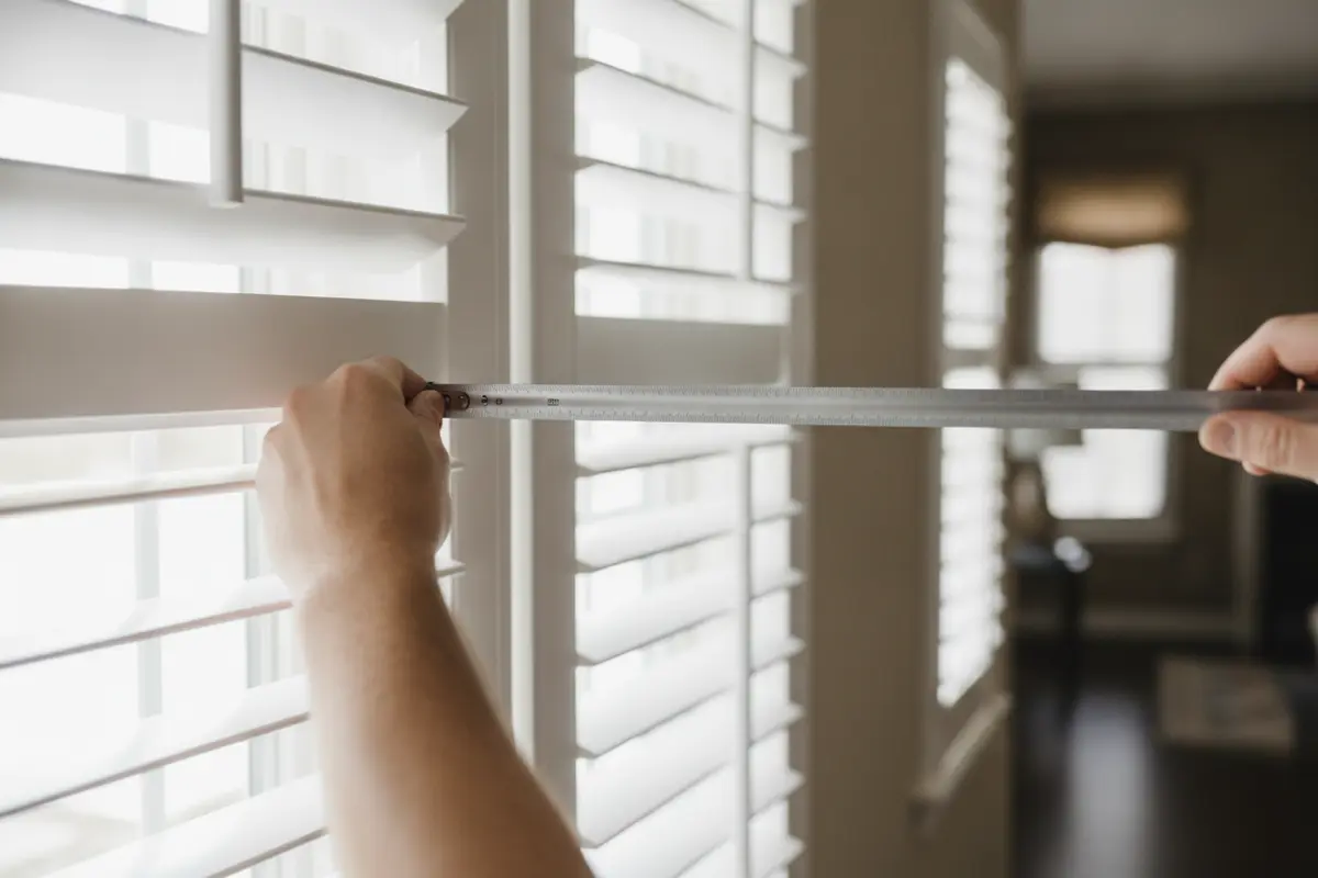 A professional measuring a window frame for custom composite plantation shutters