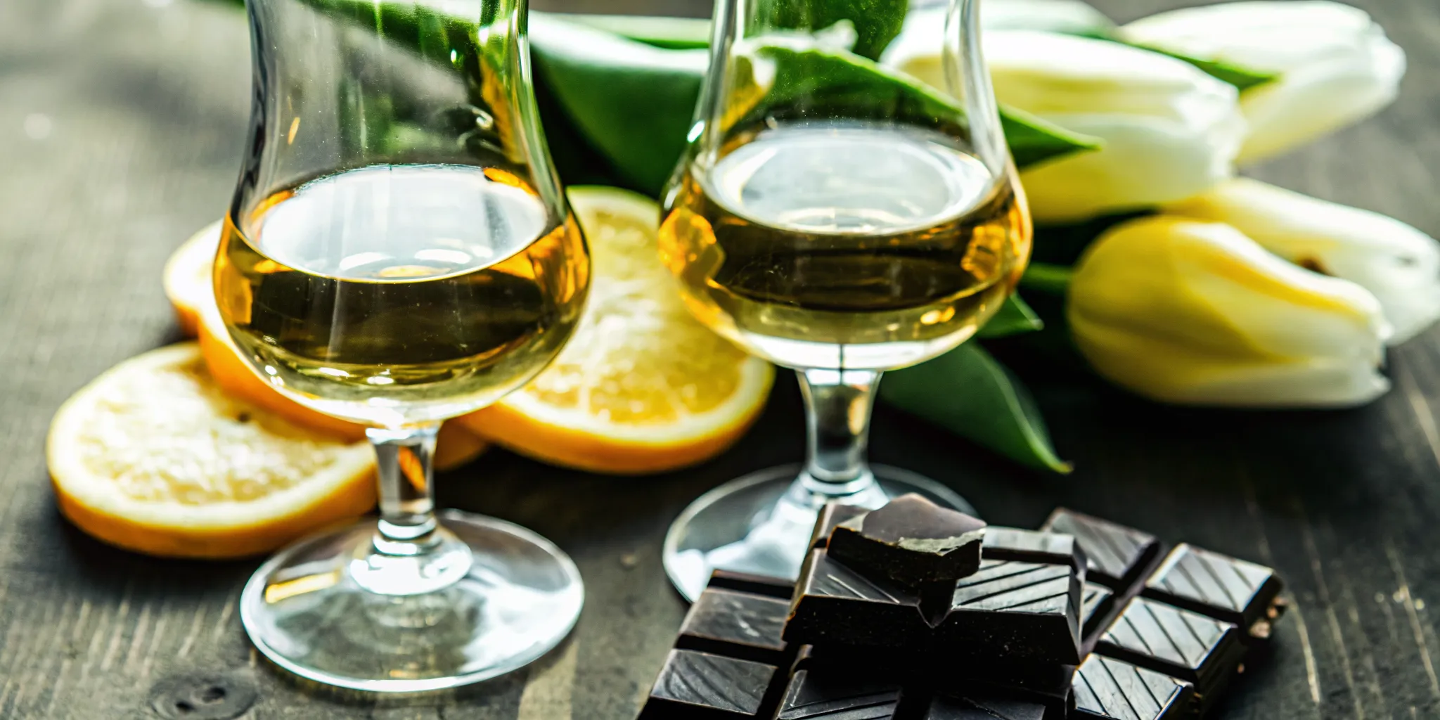 Premium tequila tasting setup with tulip glasses, sliced citrus, dark chocolate, and nuts on a wooden table