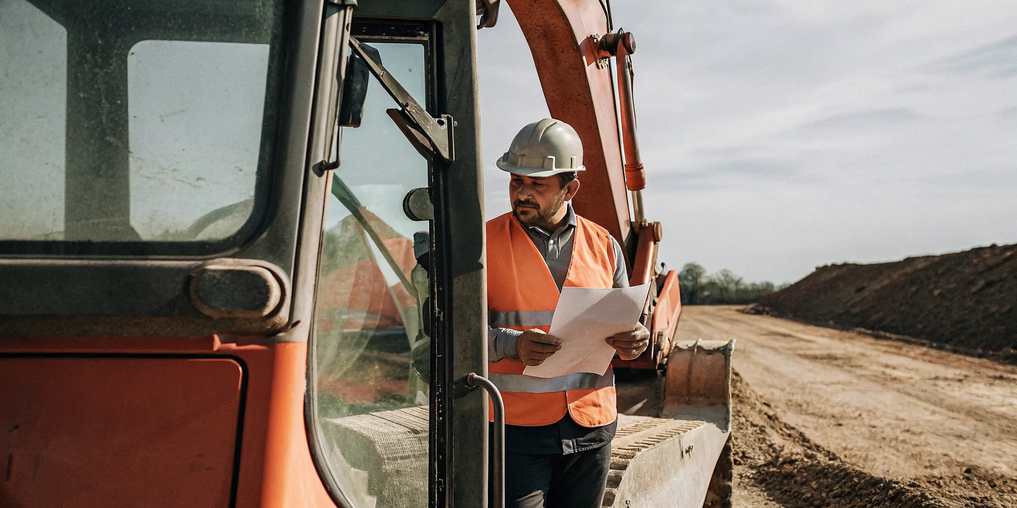 Operator reviewing Massachusetts hoisting license application documents beside excavator