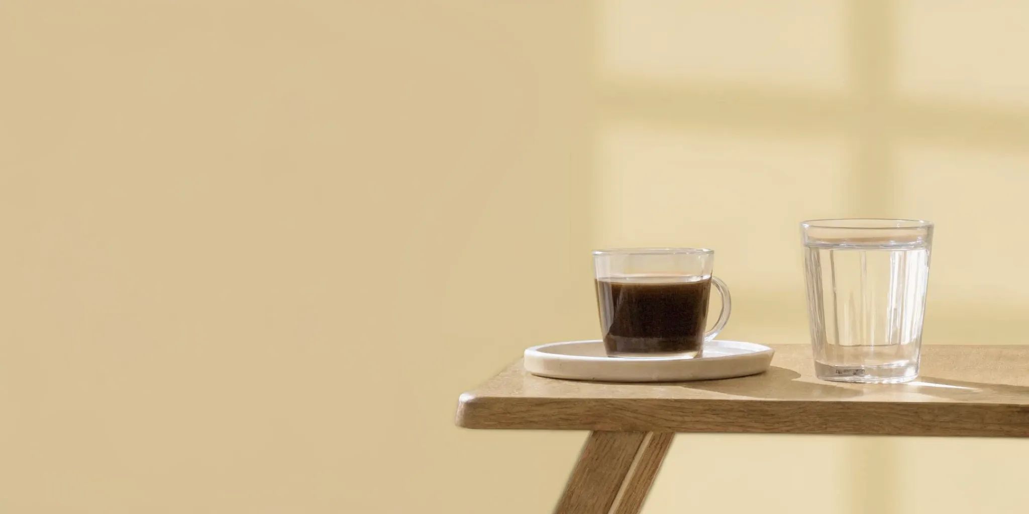 A steaming cup of dark roast coffee on a minimalist wooden table next to a fresh glass of water, showing low-acid brewing options for digestive support.
